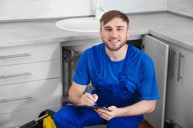 Photo of Professional plumber in uniform with clipboard near kitchen sink