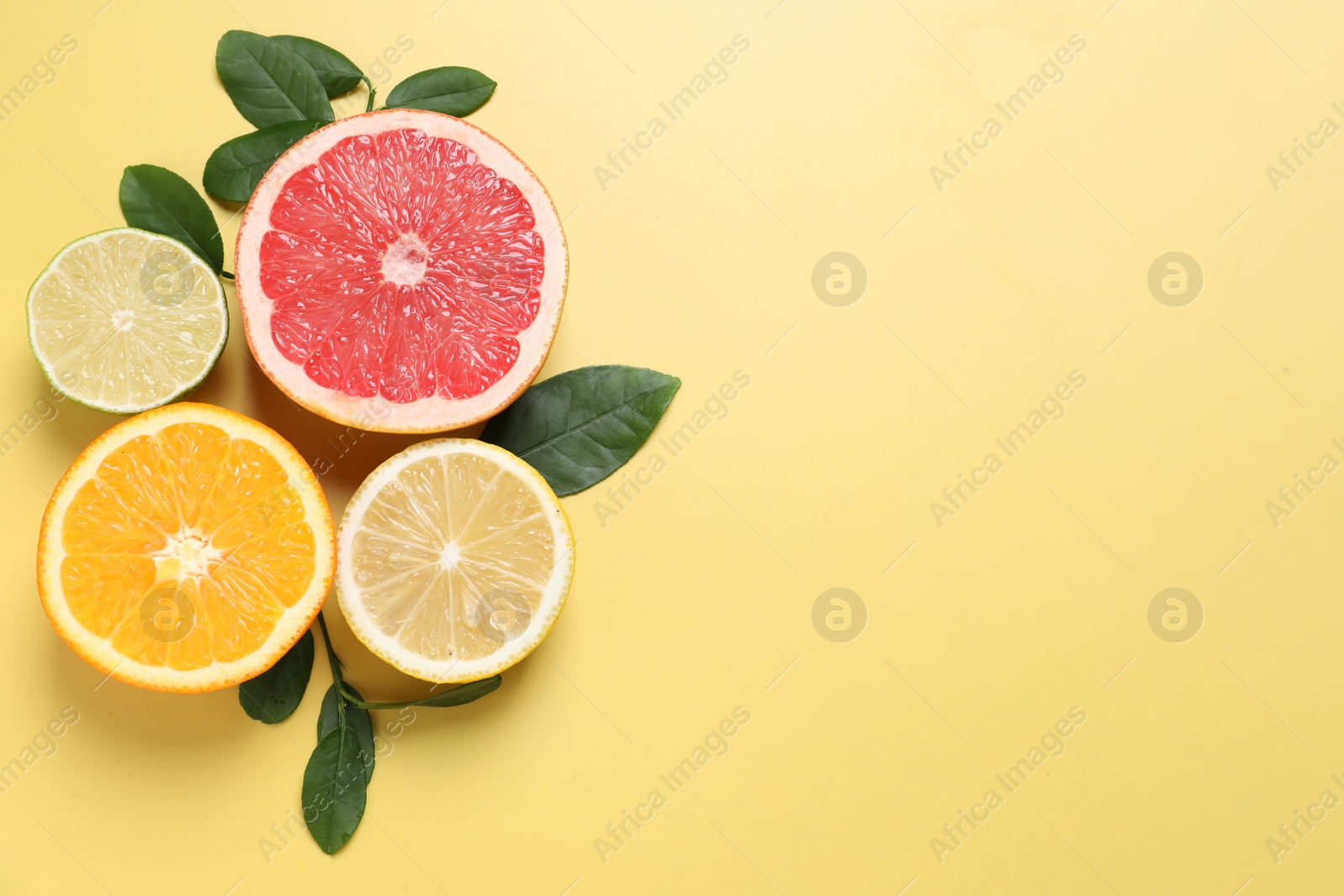 Photo of Different cut citrus fruits and leaves on yellow table, flat lay. Space for text