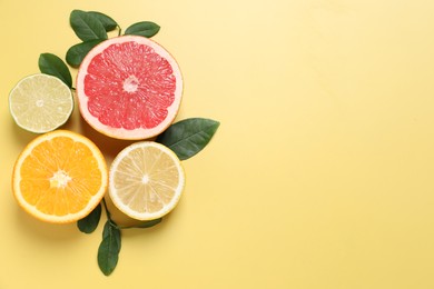 Different cut citrus fruits and leaves on yellow table, flat lay. Space for text