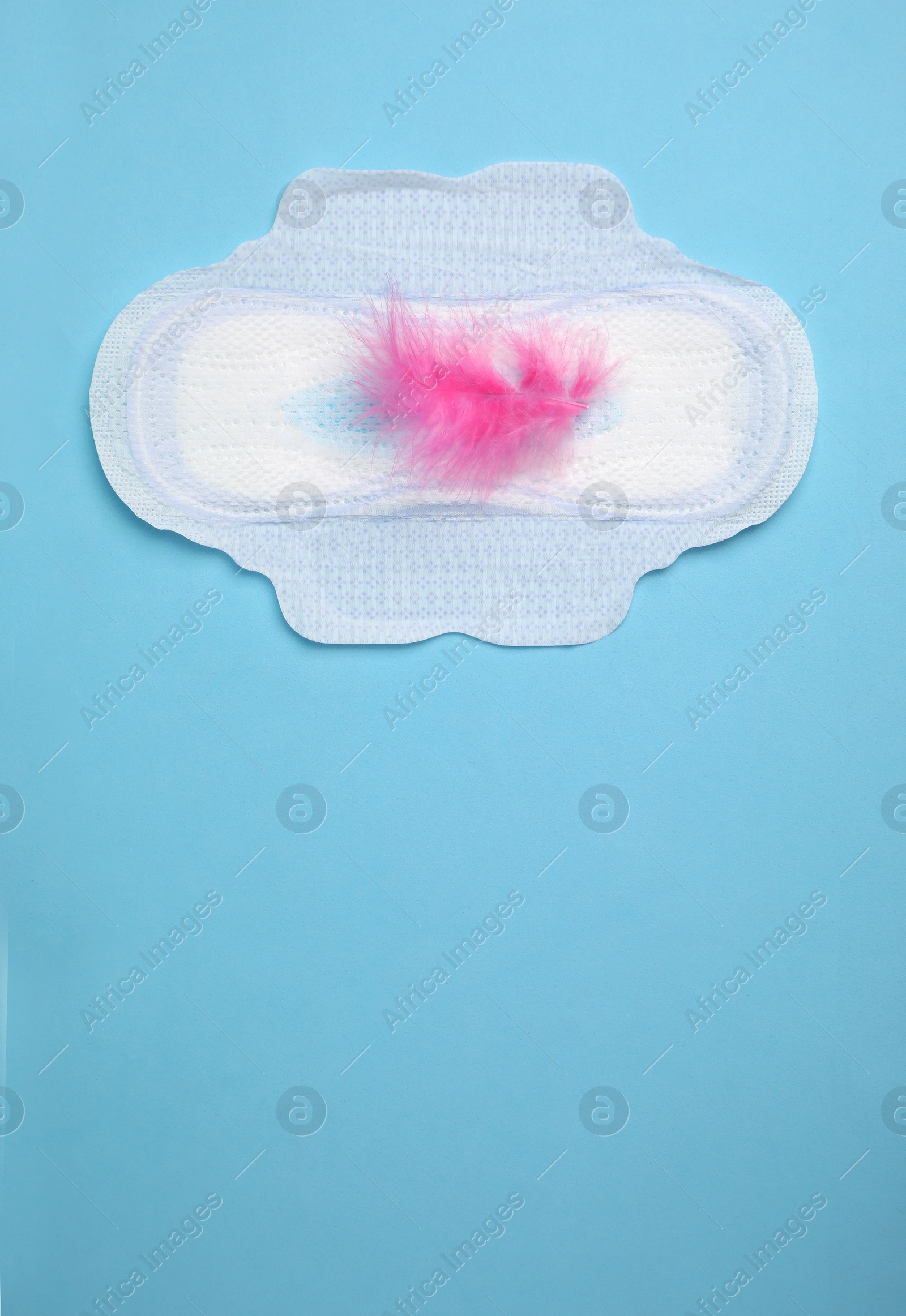 Photo of Menstrual pad with pink feather on light blue background, top view. Space for text