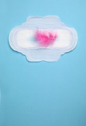 Photo of Menstrual pad with pink feather on light blue background, top view. Space for text