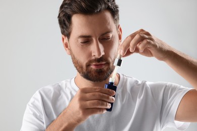 Handsome man opening cosmetic serum on light grey background
