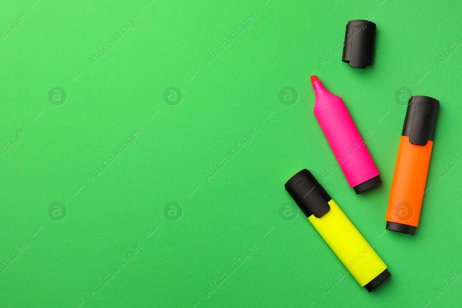 Photo of Bright color markers on green background, flat lay. Space for text