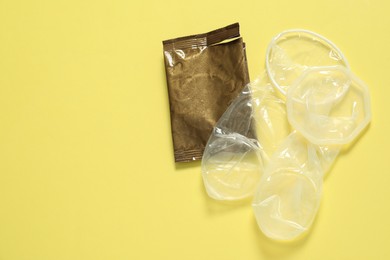 Unrolled female condoms and torn package on yellow background, flat lay with space for text. Safe sex