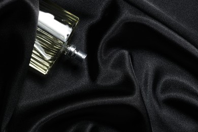 Photo of Luxury men's perfume in bottle on black satin fabric, top view. Space for text