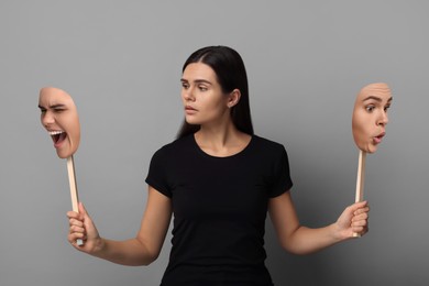 Image of Woman holding masks with her face showing different emotions on grey background. Balanced personality