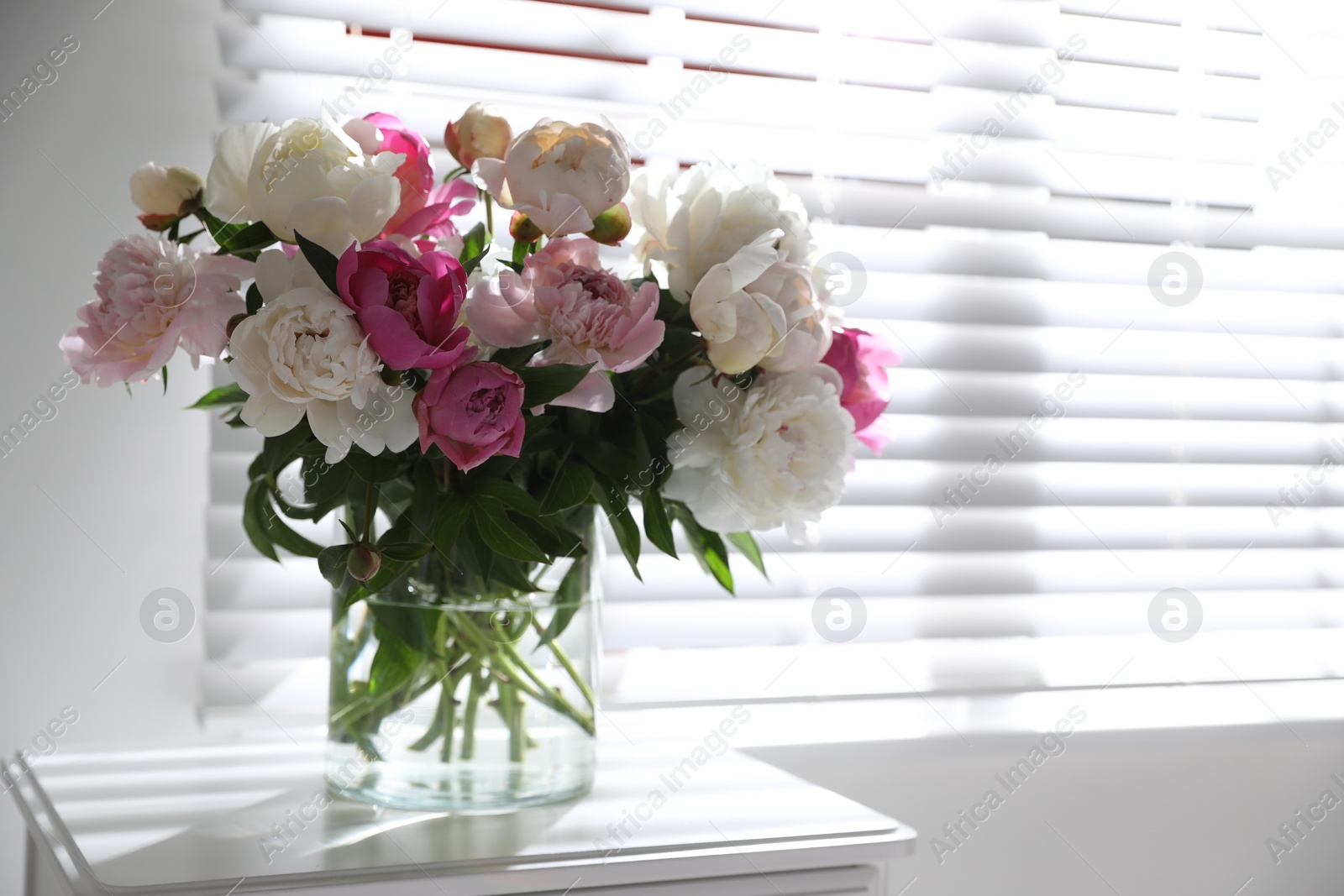 Photo of Beautiful peonies in vase on table near window indoors. Space for text