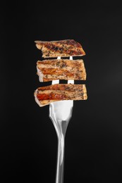 Photo of Meat fork with pieces of delicious grilled pork steak against black background