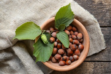 Tasty hazelnuts and green leaves on wooden table, top view. Healthy snack