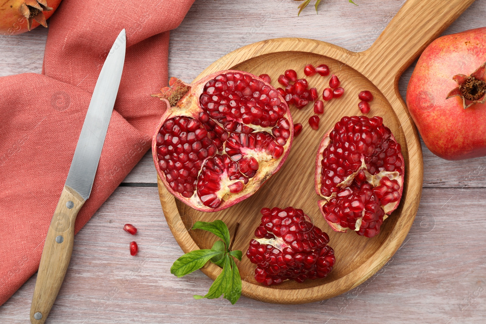 Photo of Fresh pomegranates, green leaves and knife on wooden table, flat lay