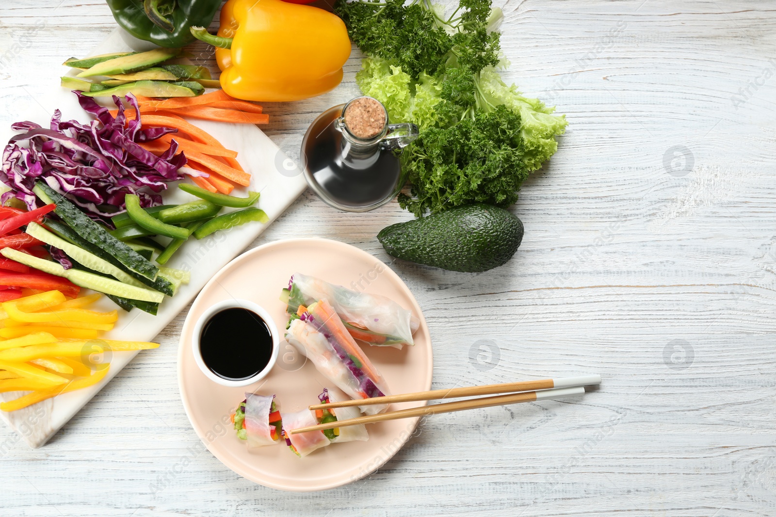 Photo of Delicious rolls wrapped in rice paper served on white wooden table, flat lay