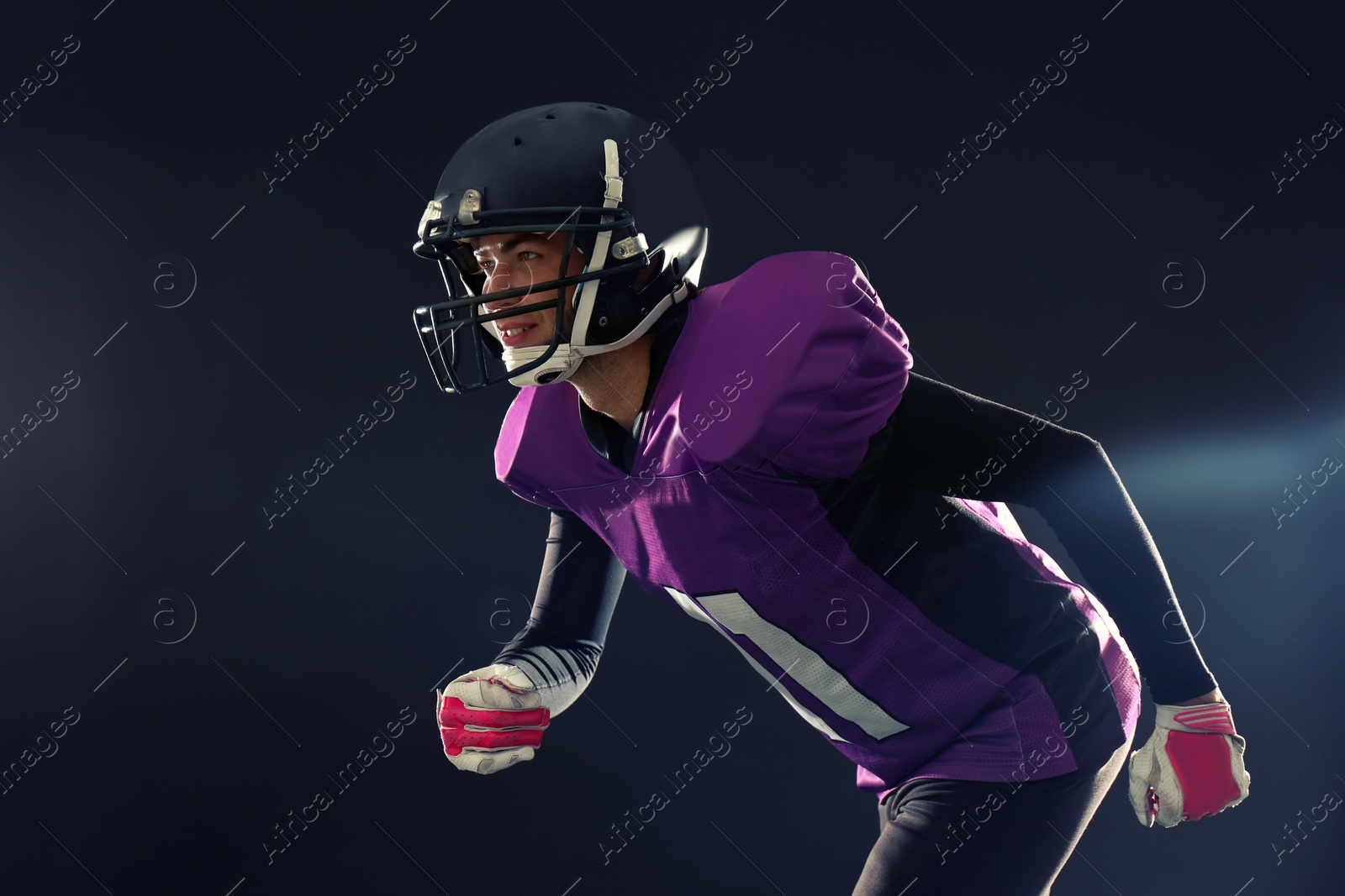 Photo of American football player in uniform running on dark background