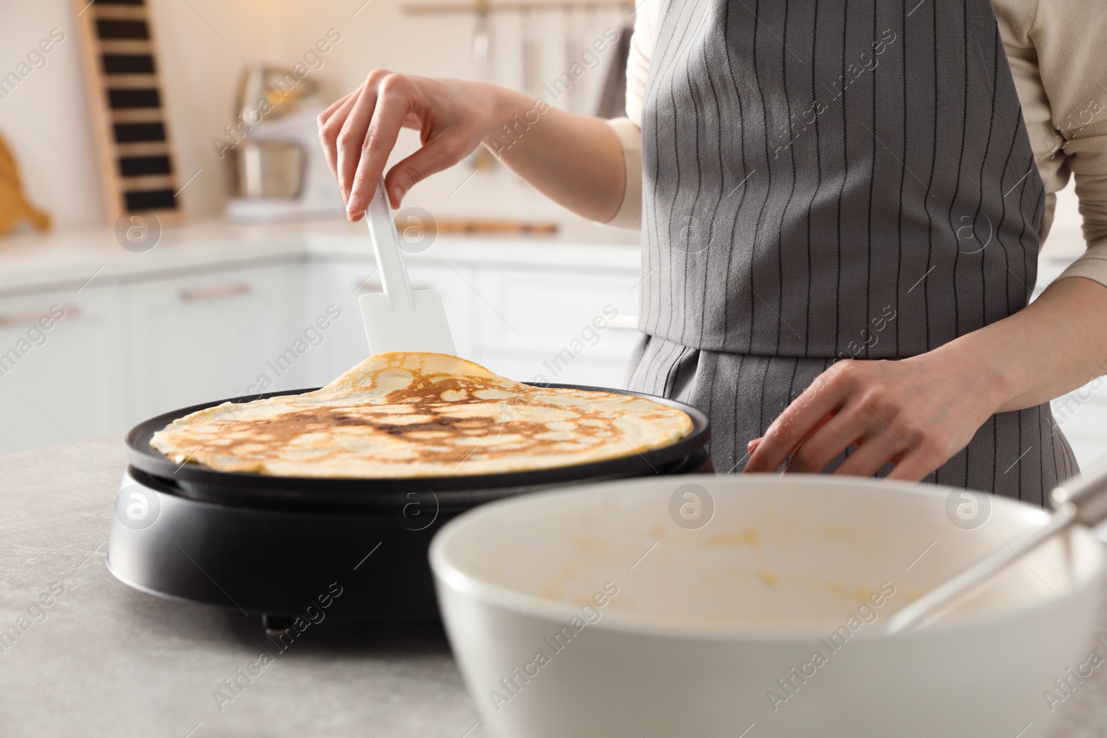 Photo of Woman cooking delicious crepe on electric pancake maker in kitchen, closeup