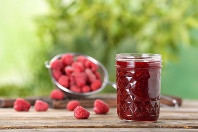 Photo of Jar with raspberry jam on table against blurred background