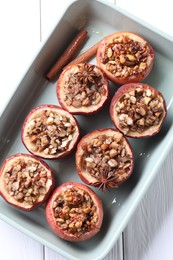 Photo of Tasty baked apples with nuts, honey and spices in dish on white wooden table, top view