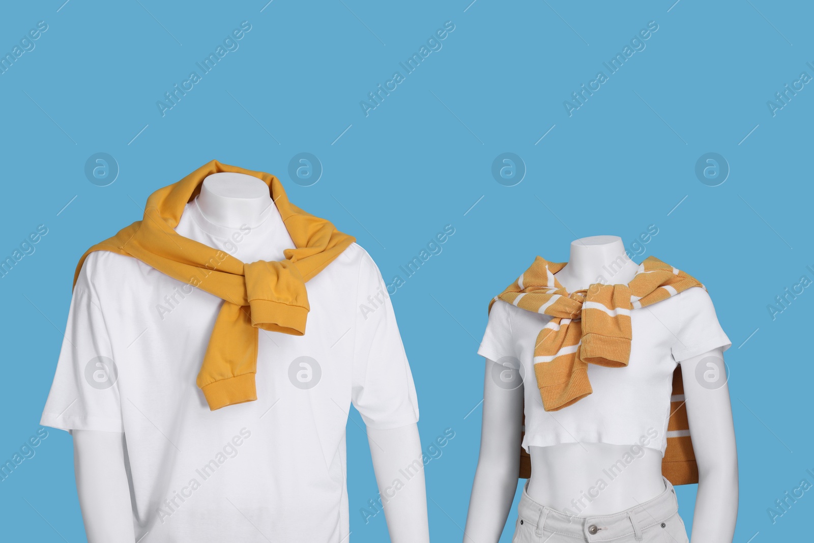 Photo of Female and male mannequins dressed in white t-shirts and orange sweaters on light blue background