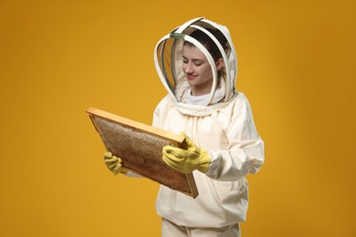 Beekeeper in uniform holding hive frame with honeycomb on yellow background