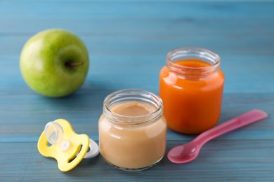 Photo of Jars with healthy baby food, apple, pacifier and spoon on light blue wooden table