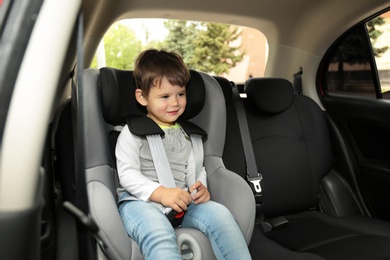 Photo of Cute little child sitting in safety seat inside car. Danger prevention