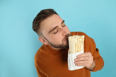 Young man with delicious shawarma on turquoise background