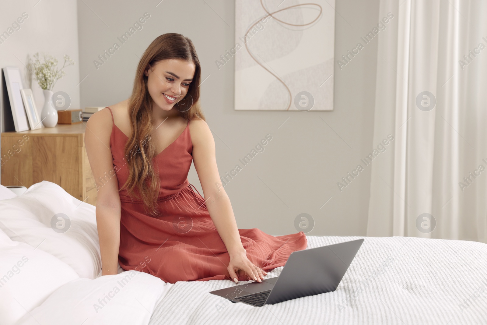 Photo of Happy woman with laptop on bed in bedroom