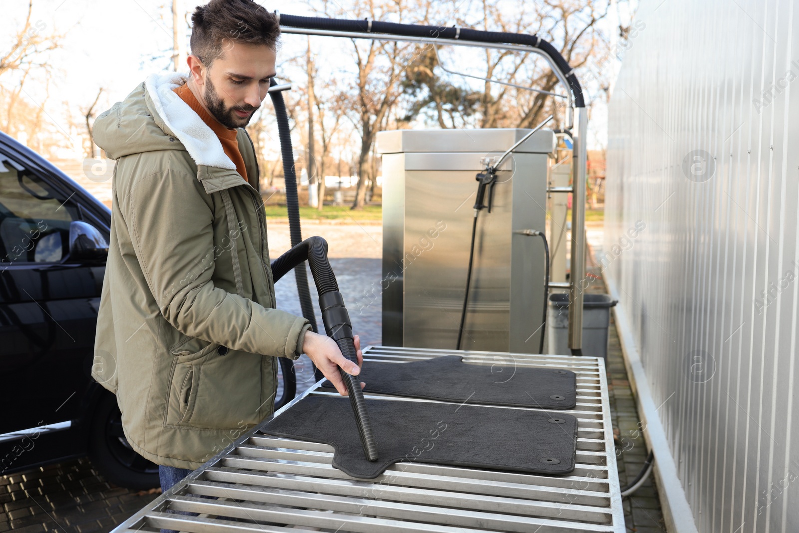 Photo of Man cleaning auto carpets with vacuum cleaner at self-service car wash