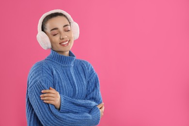 Beautiful young woman wearing earmuffs on pink background. Space for text