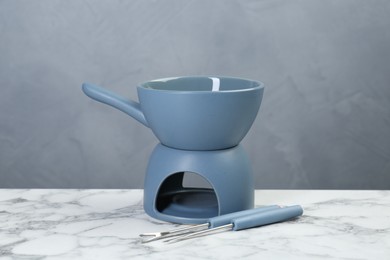 Photo of Fondue set on white marble table against light gray wall