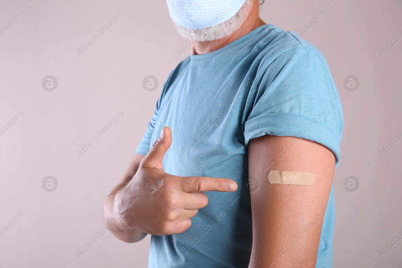 Photo of Senior man in protective mask pointing at arm with bandage after vaccination on beige background, closeup