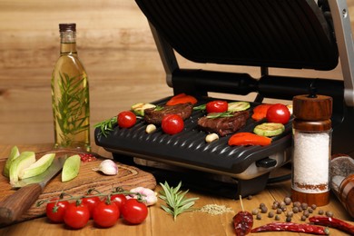 Electric grill with different products and knife on wooden table