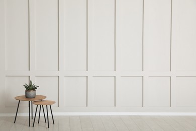 Tables with potted houseplant near empty wall indoors. Space for design