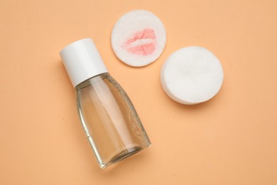 Photo of Bottle of makeup remover, clean and dirty cotton pads on pale orange background, flat lay