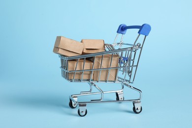Photo of Small metal shopping cart with cardboard boxes on light blue background