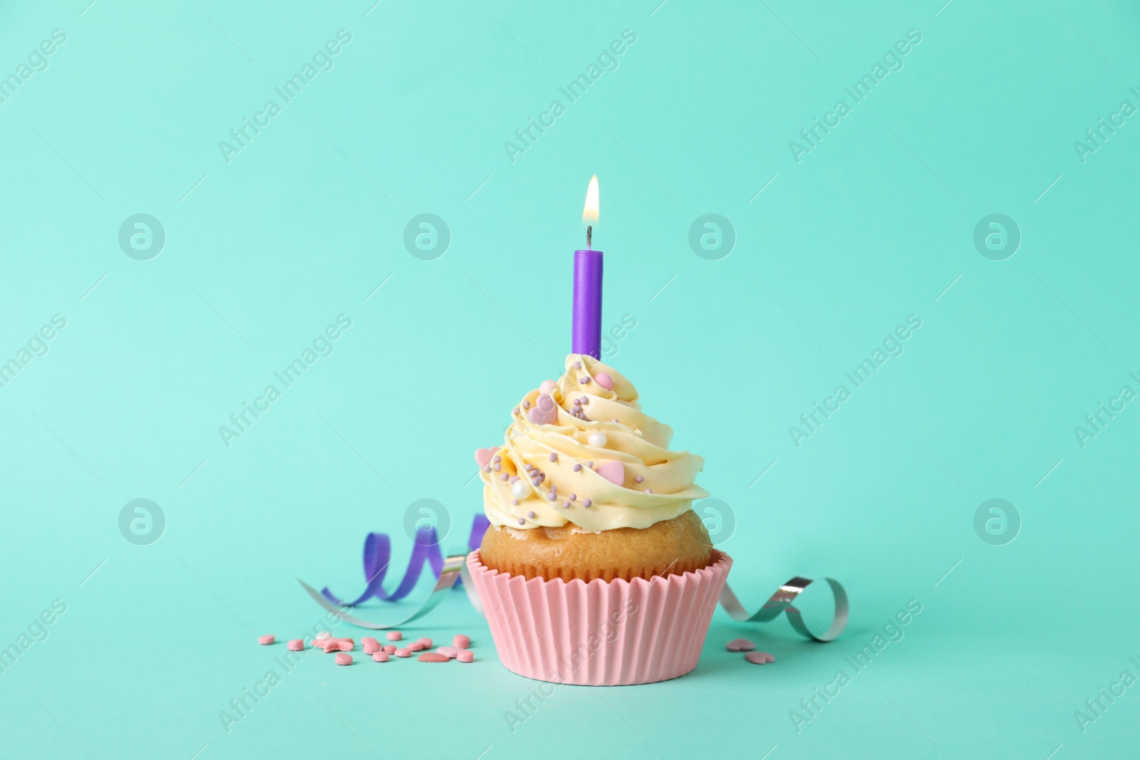 Photo of Birthday cupcake with burning candle and sprinkles on turquoise background