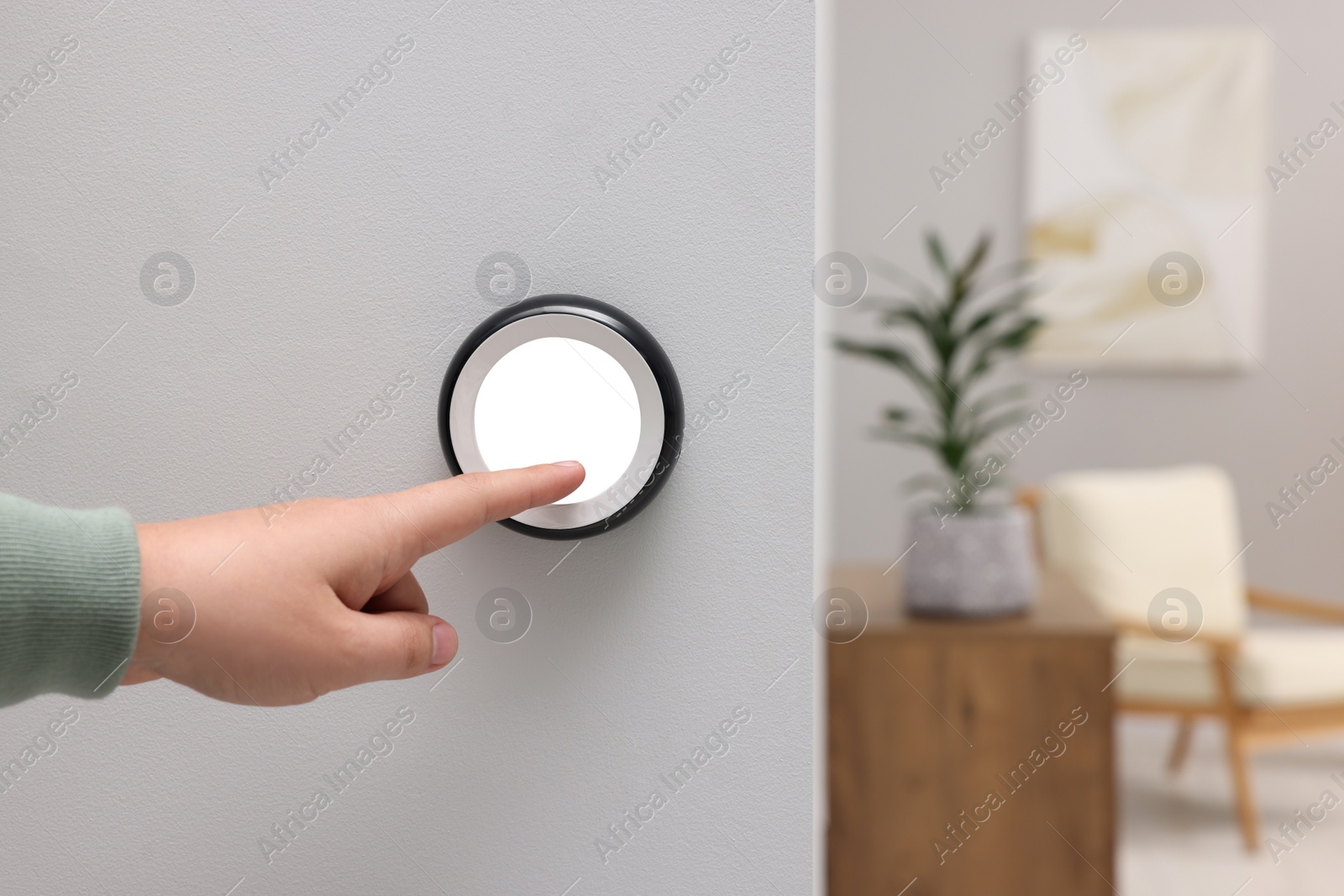 Photo of Man adjusting thermostat on white wall indoors, closeup. Smart home system