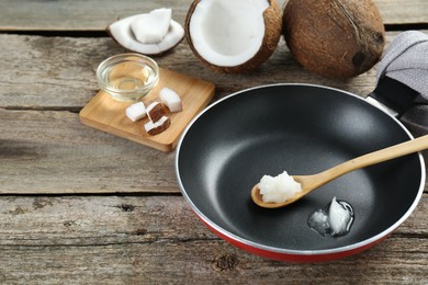 Frying pan with organic coconut cooking oil and spoon on wooden table, space for text