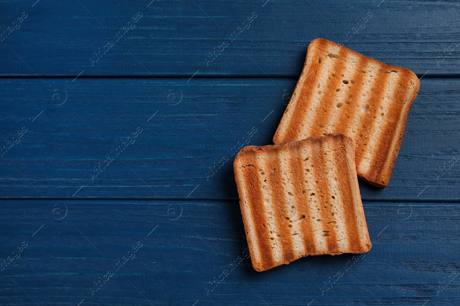 Photo of Slices of delicious toasted bread on blue wooden table, top view. Space for text