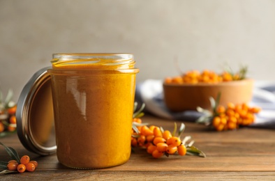 Photo of Delicious sea buckthorn jam and fresh berries on wooden table. Space for text