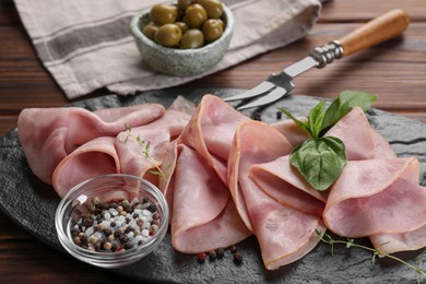 Photo of Tasty ham with basil, sea salt, peppercorns and carving fork on wooden table, closeup