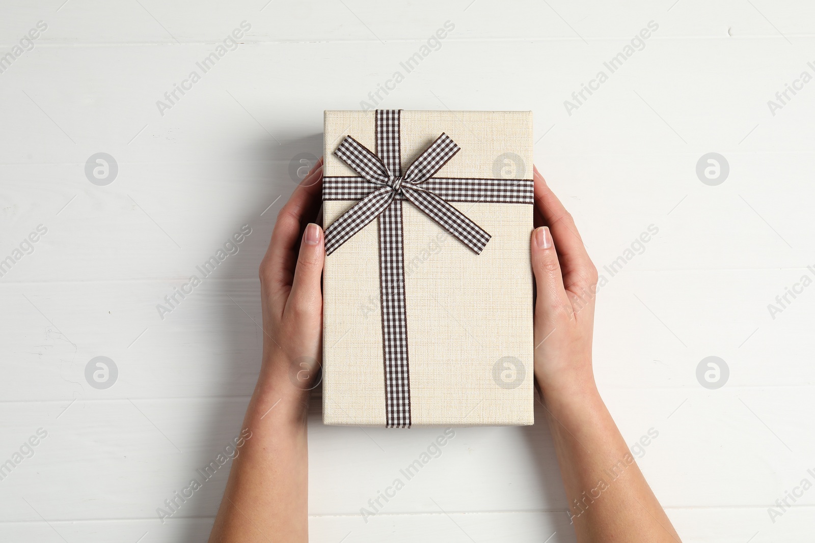 Photo of Woman holding gift box at white wooden table, top view