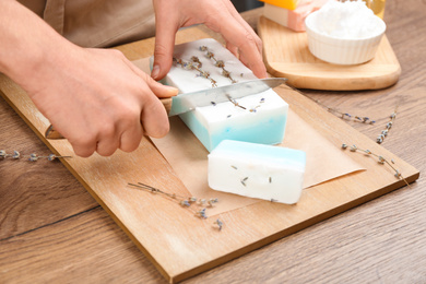 Photo of Woman cutting natural handmade soap on wooden table, closeup