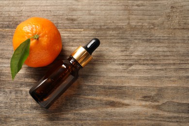 Bottle of tangerine essential oil and fresh fruit on wooden table, flat lay. Space for text