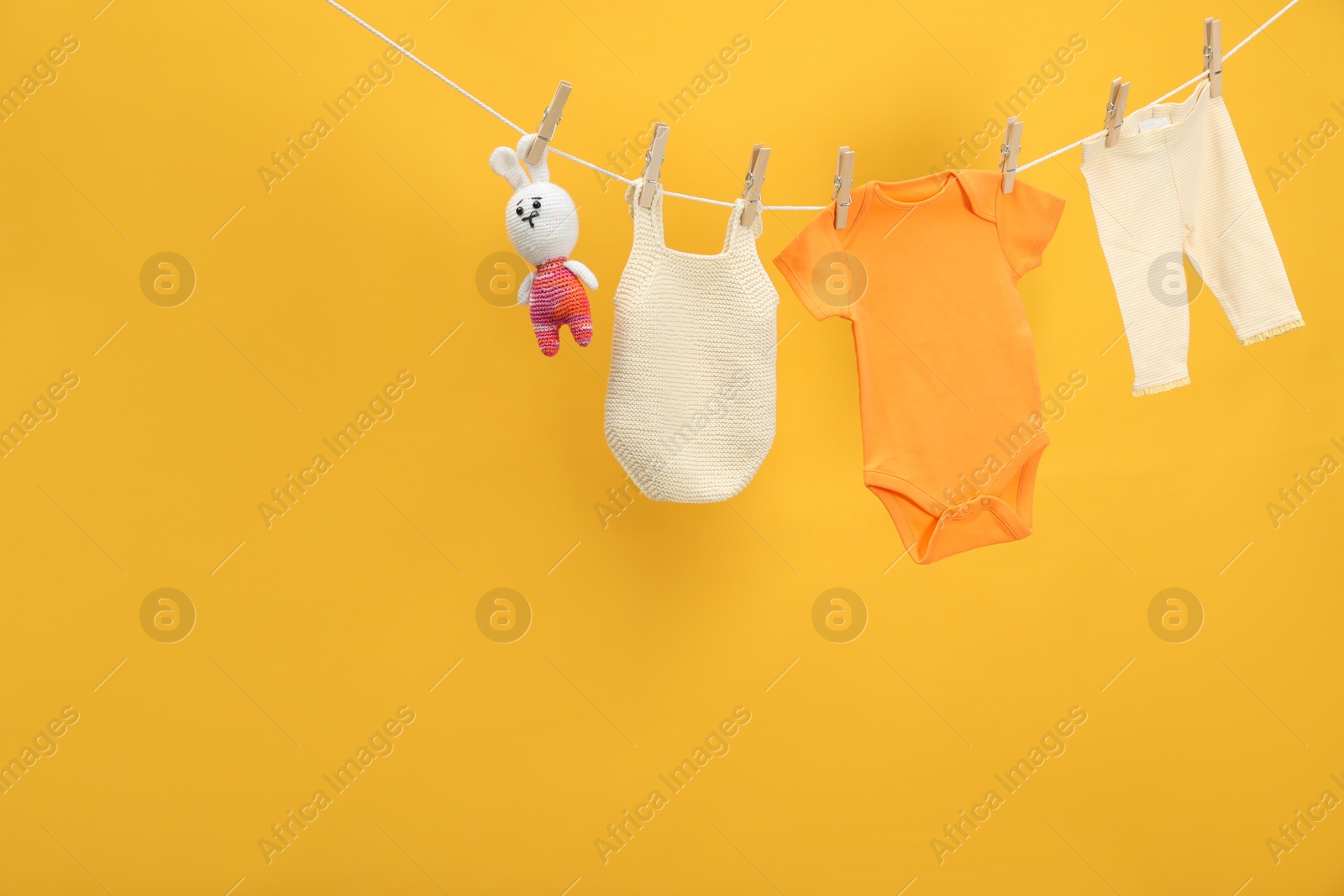 Photo of Different baby clothes and bunny toy drying on laundry line against orange background. Space for text