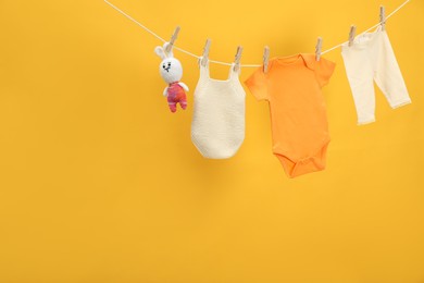 Photo of Different baby clothes and bunny toy drying on laundry line against orange background. Space for text