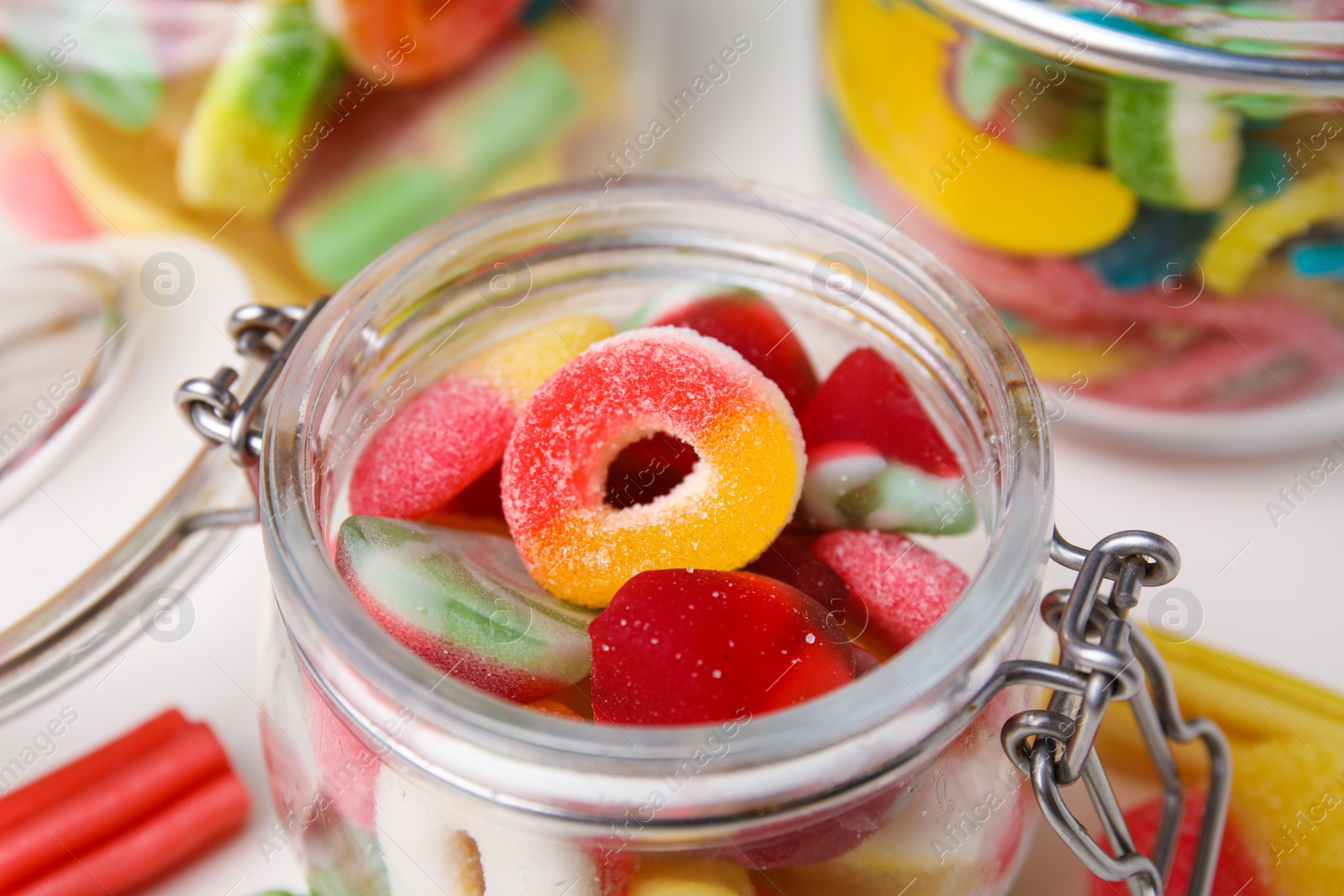 Photo of Tasty jelly candies in jars on white table, closeup