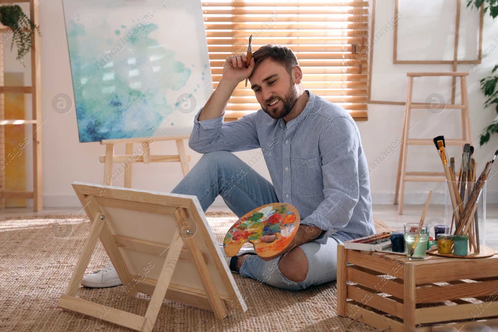 Photo of Young man painting on easel with brush in artist studio