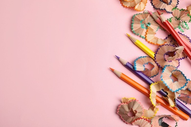 Photo of Color pencils and shavings on pink background, top view. Space for text