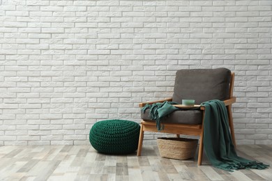 Photo of Stylish knitted pouf and comfortable armchair near white brick wall indoors, space for text. Interior design