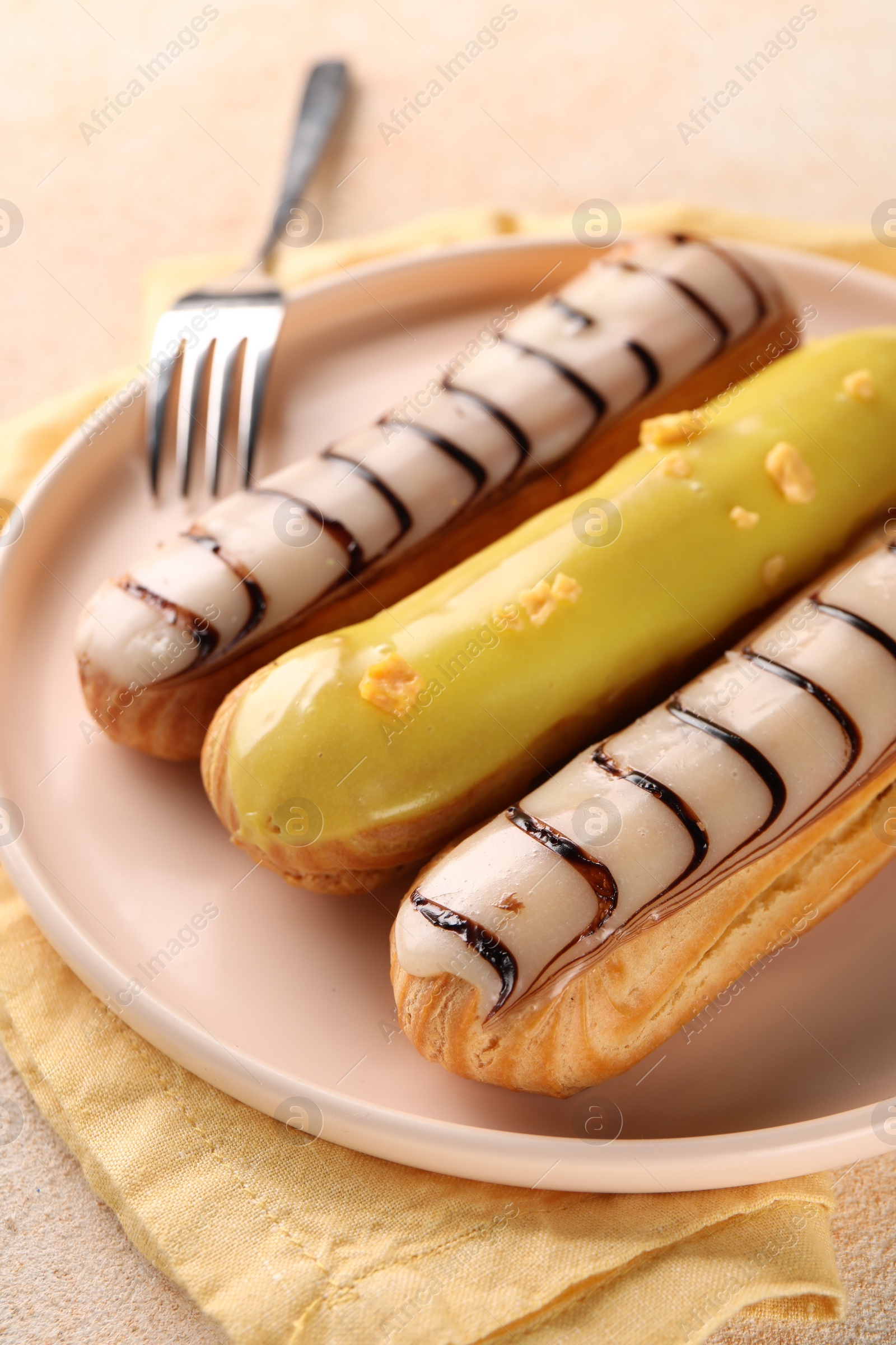 Photo of Different tasty glazed eclairs served on color textured table, closeup