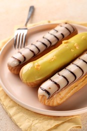 Different tasty glazed eclairs served on color textured table, closeup